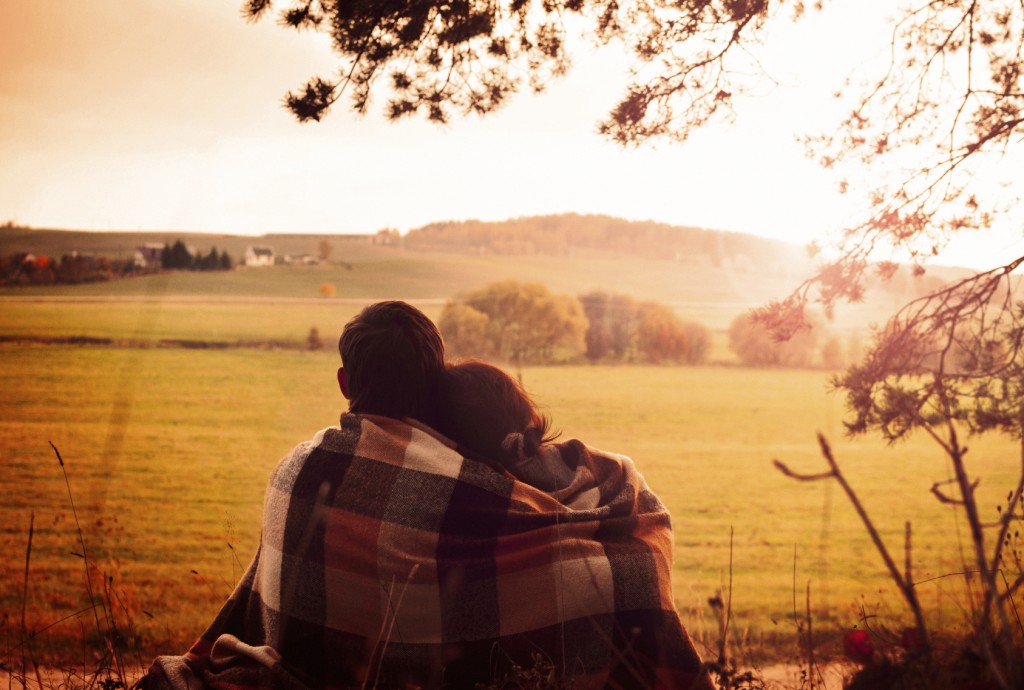 Young couple sitting back having covered with coverlet and enjoy the scenery on the edge of the forest