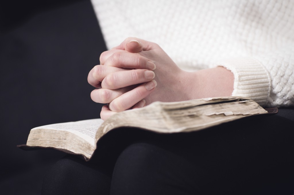 Christian woman pray and folding hands over the holy bible.