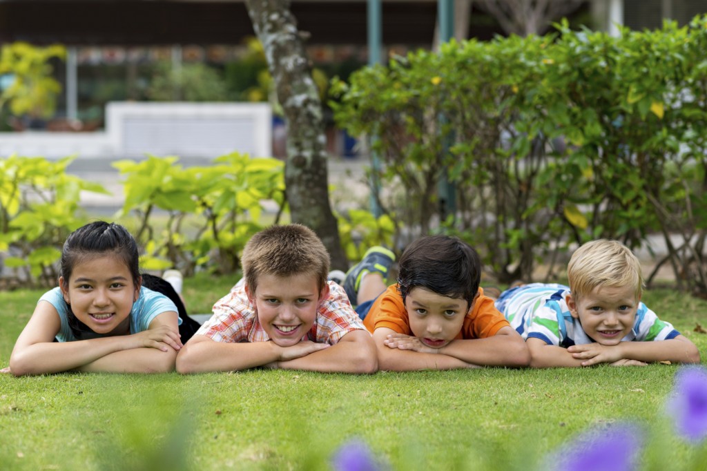 Group of four cheerful kids lying on the stomachs on the grass in the park