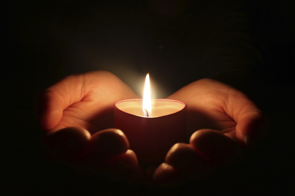 hands holding one candle in darkness