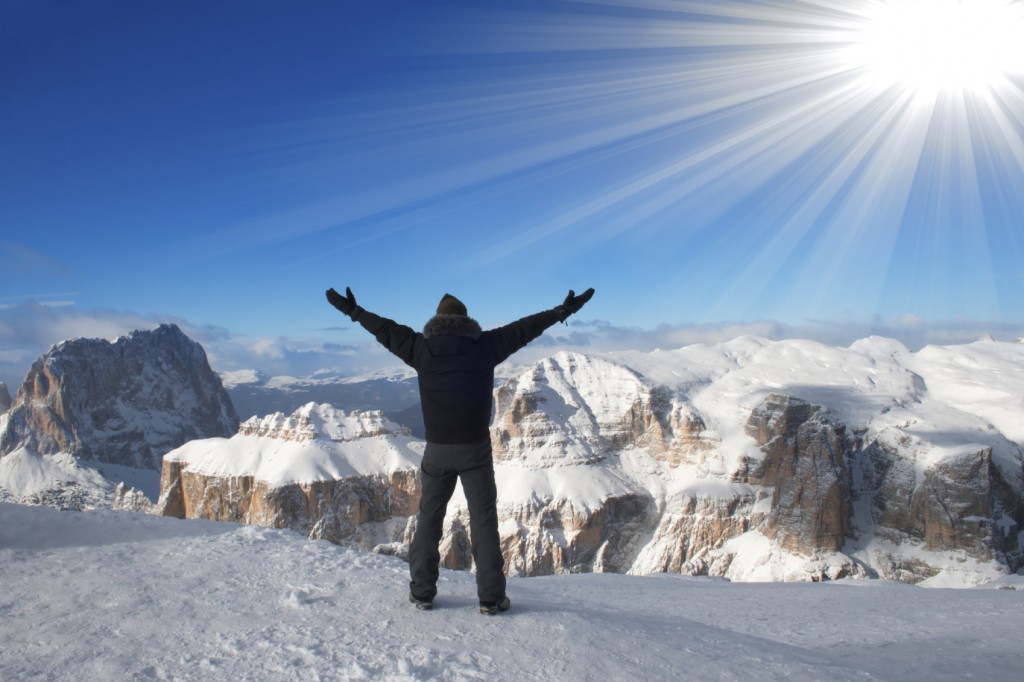 A man triumphantly raising his hands over his head watching the beautiful view of snow-capped mountains