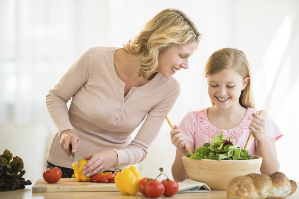 Happy little girl assisting mother in preparing food at kitchen counter
