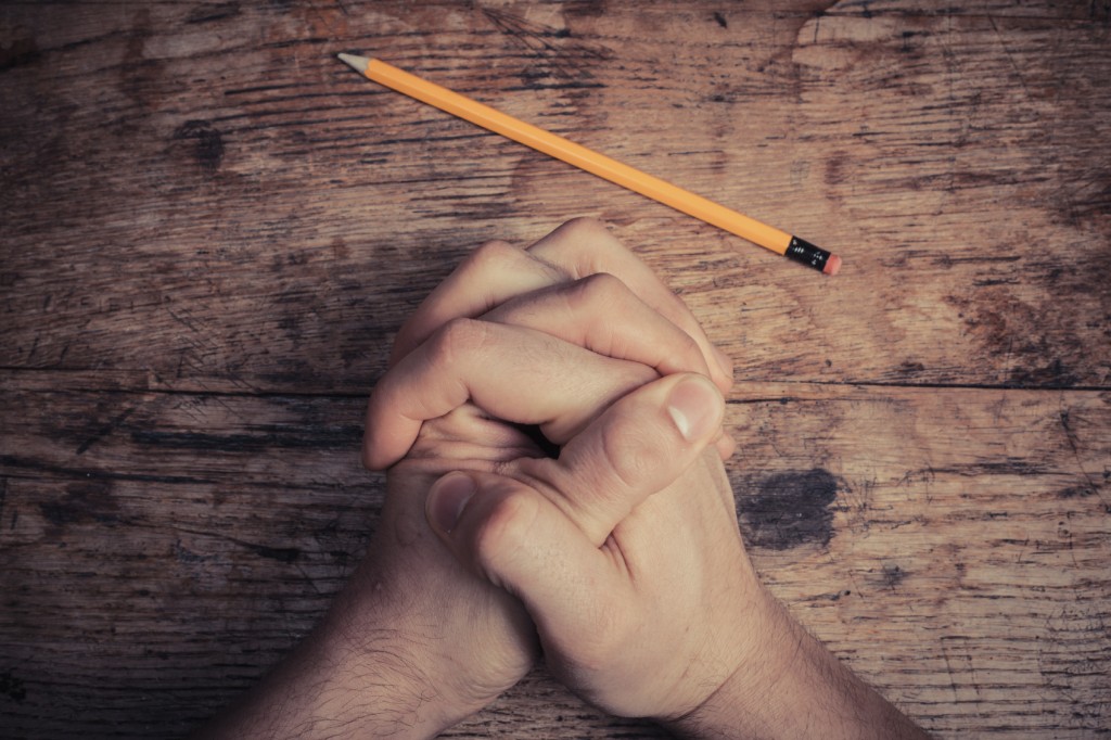 Hands folded in prayer on table with pencil