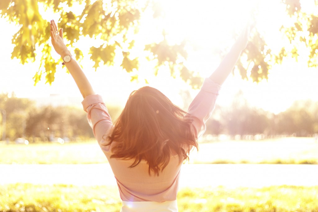 Woman standing in sunlight with arms up