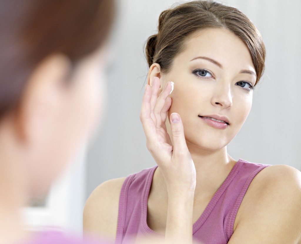 Woman caring of her beautiful skin on the face standing near mirror in the bathroom