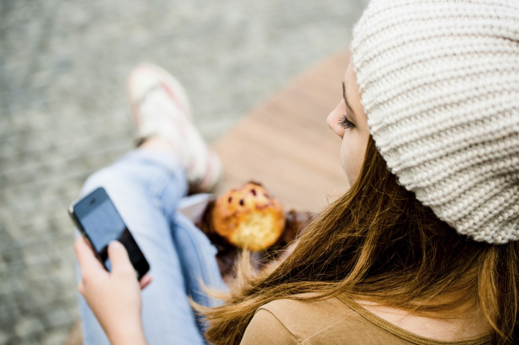 Teenager eating muffin looking in phone
