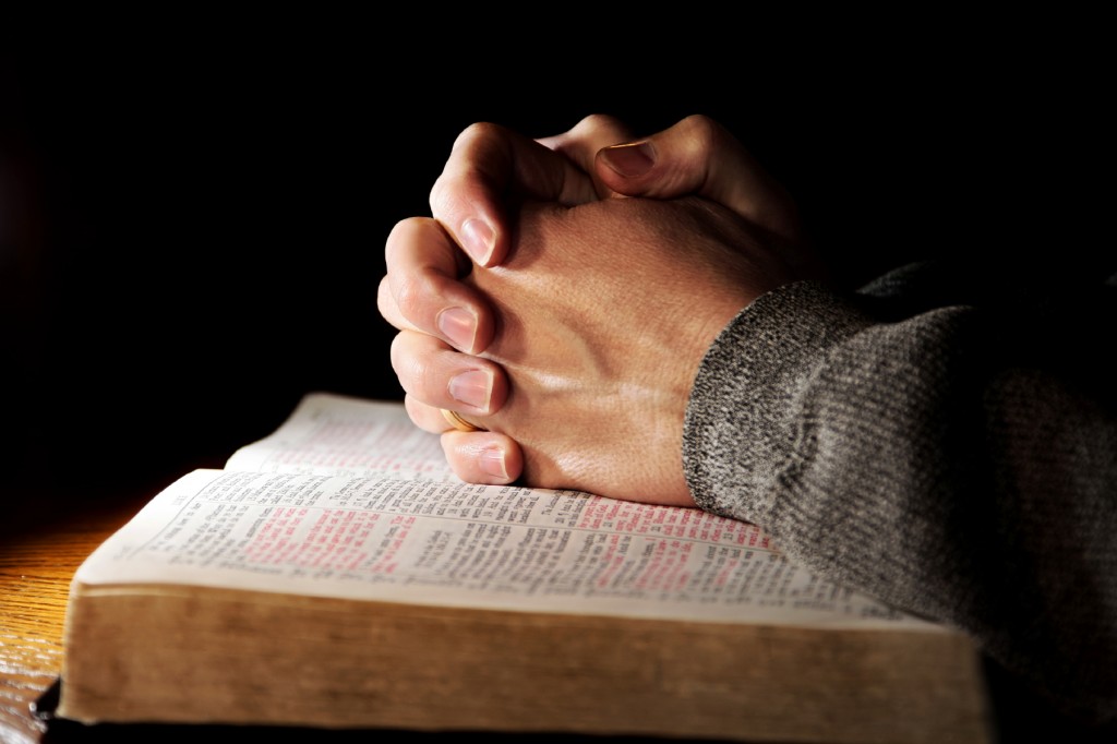 Hands of a man praying in solitude with his Bible