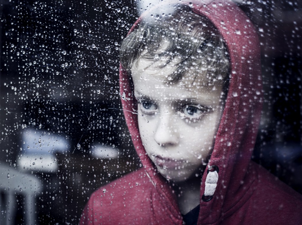 Little child looking through window. Raining outside. Depressed or sad.