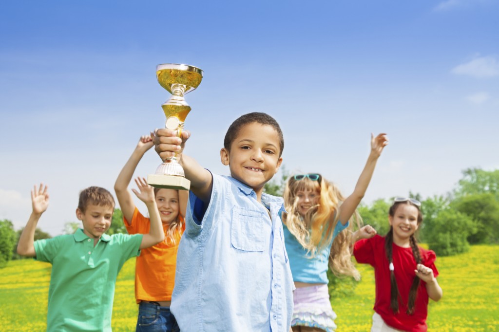 Portrait of black happy smiling little boy holding prize cup with his team on background