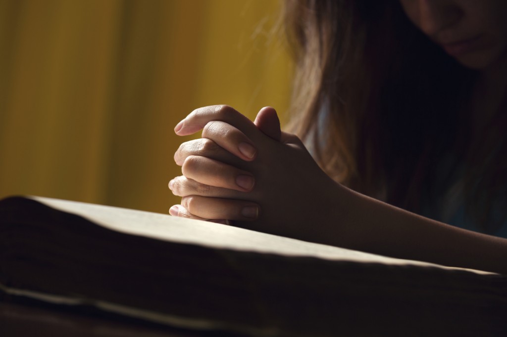 Girl Praying With Hands On Bible