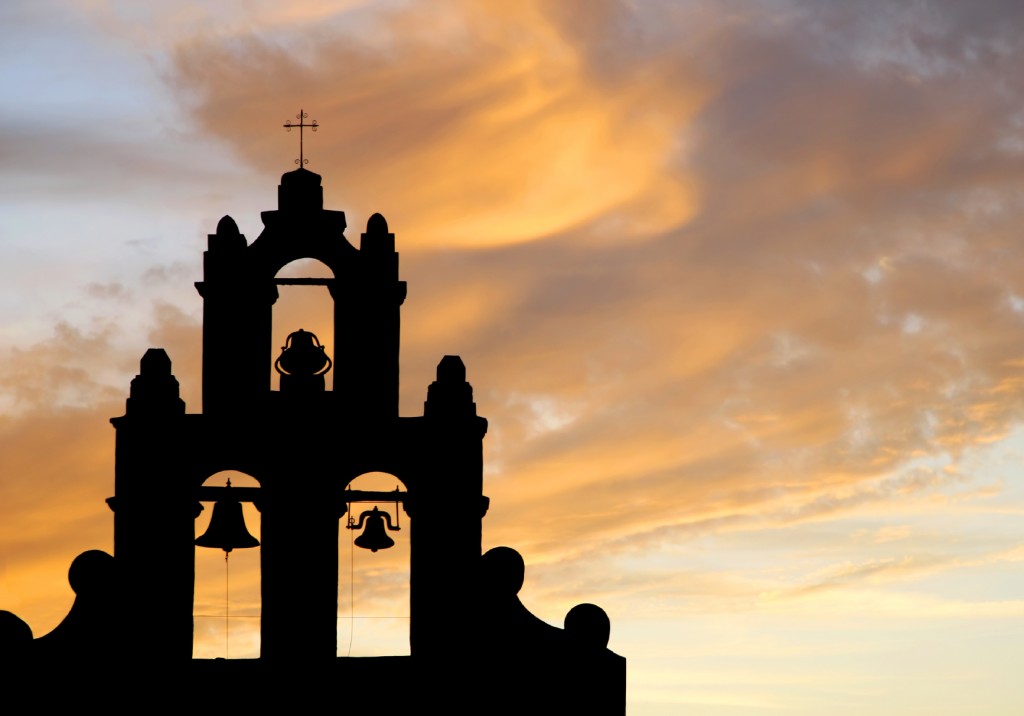 A bell tower of an authentic 1700's Spanish Mission in silhouette against a sunset sky