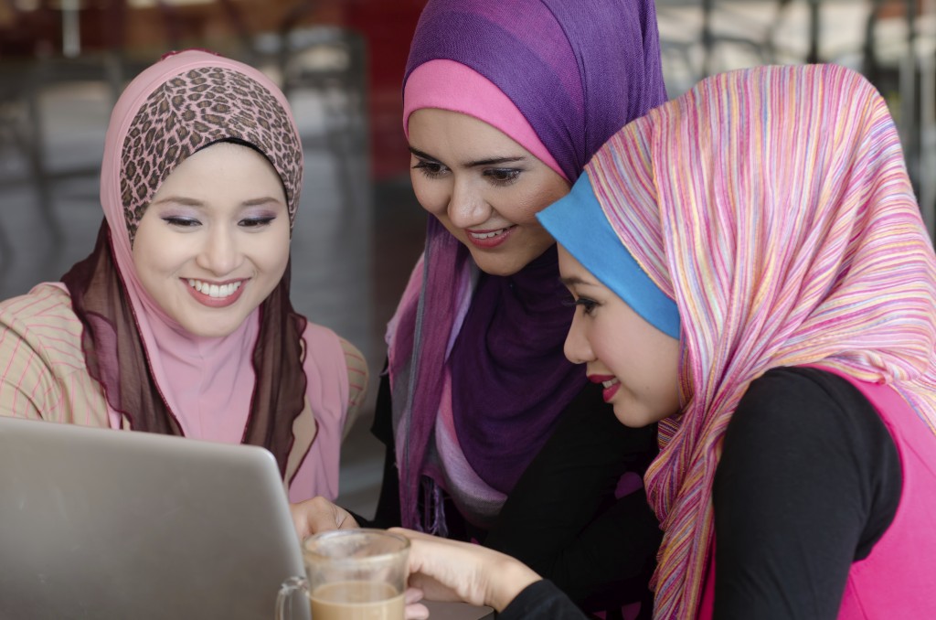 young muslim woman in head scarf using laptop in cafe with friends