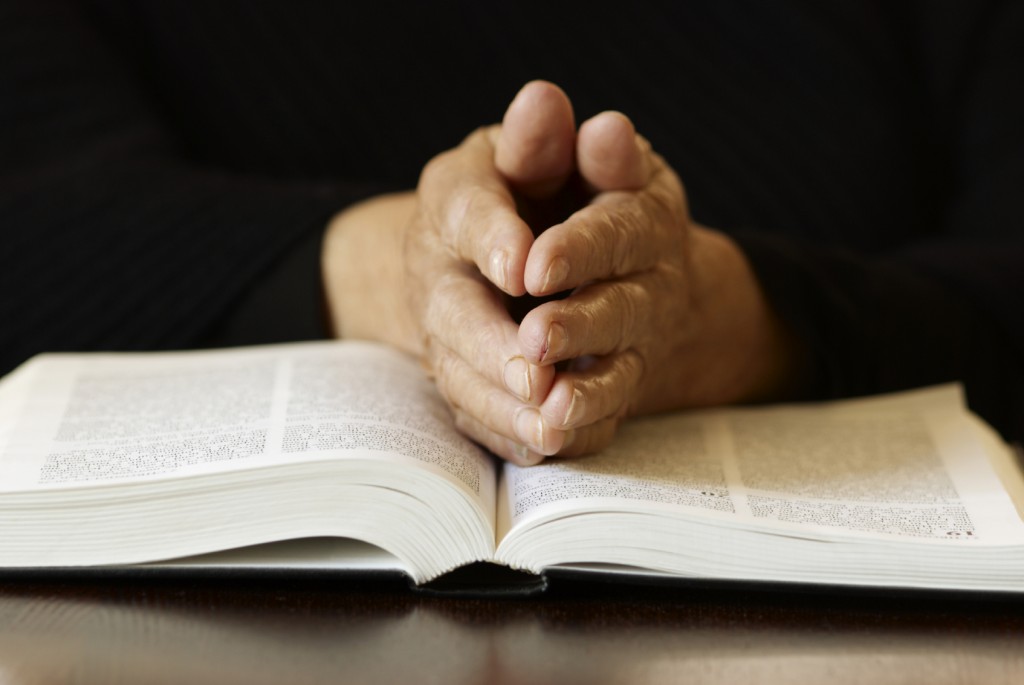 Praying hands resting on a Bible