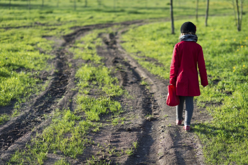 girl in red coat going far away by dirty country road,