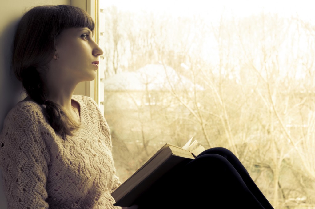 Young woman reading book near the window.