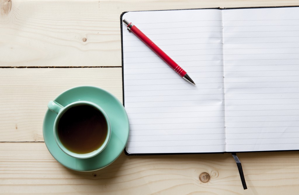 Open a blank white notebook, pen and cup of tea on the desk