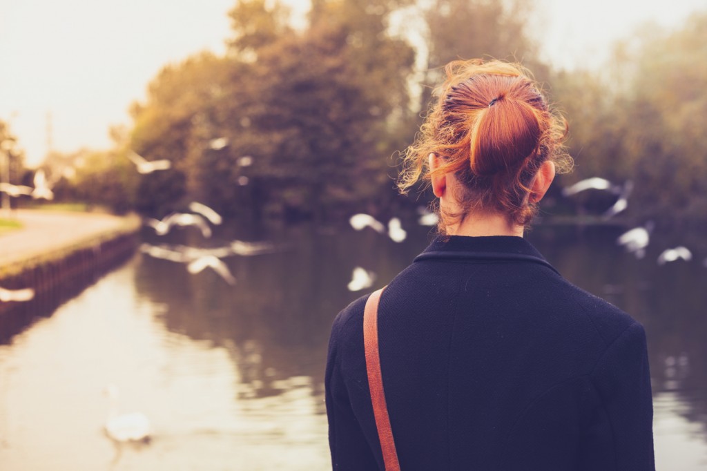 Rear view of young woman looking at birds by a river