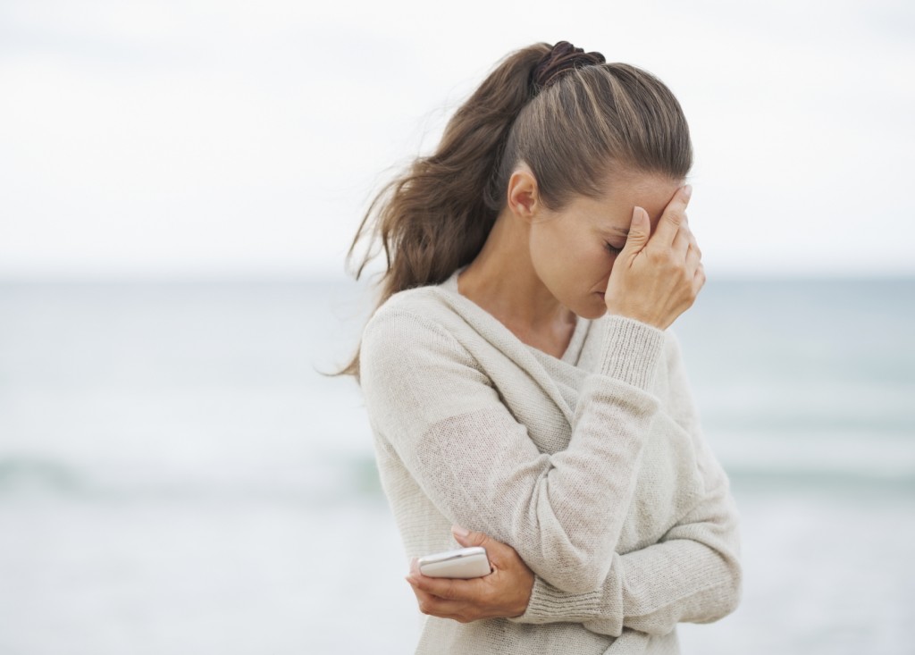 Stressed young woman in sweater on beach