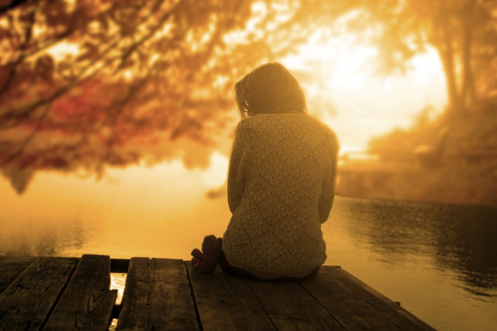 woman sitting on a dock watching the sun set in fall.