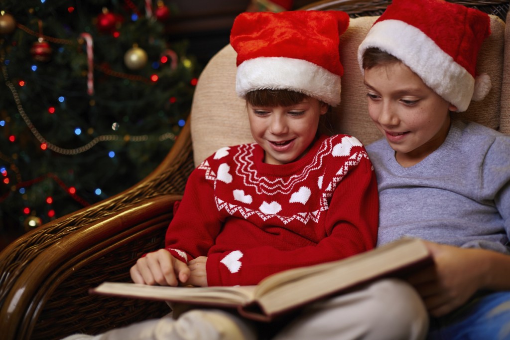 siblings in Santa caps reading book together on Christmas evening