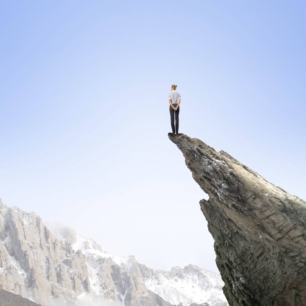 Risky businesswoman standing on edge of rock