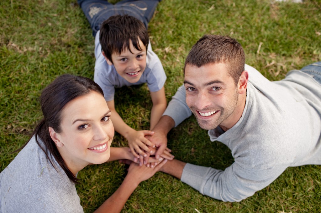 Happy parents and kid lying on garden with hands together