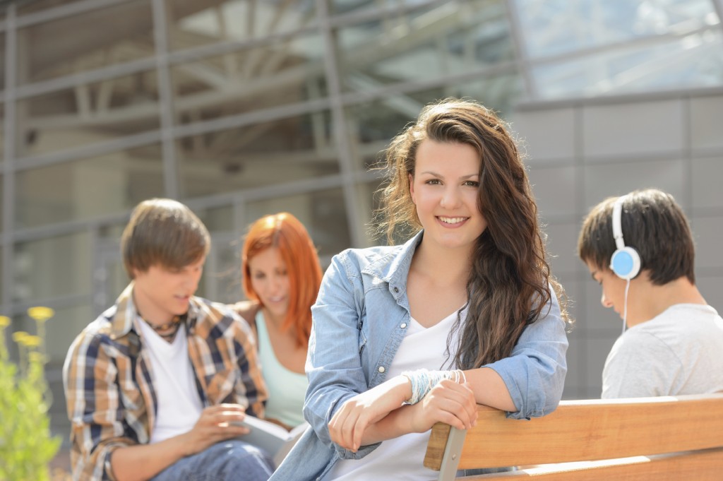 Student girl sitting on bench outside campus with friends sunny