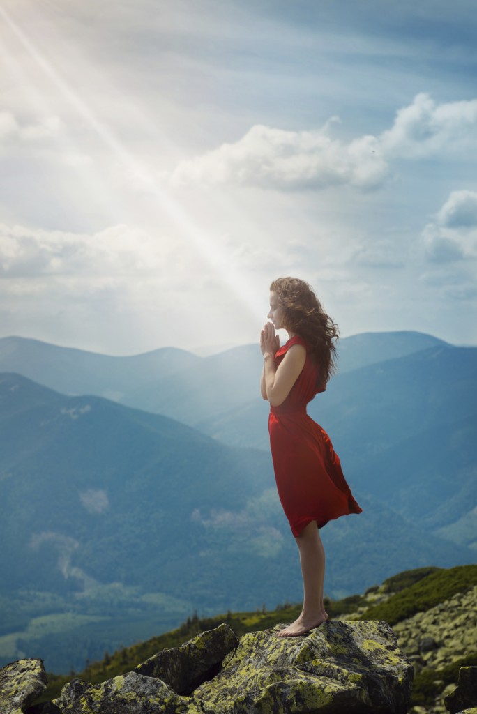 Beautiful woman in red dress standing on the stone and pray