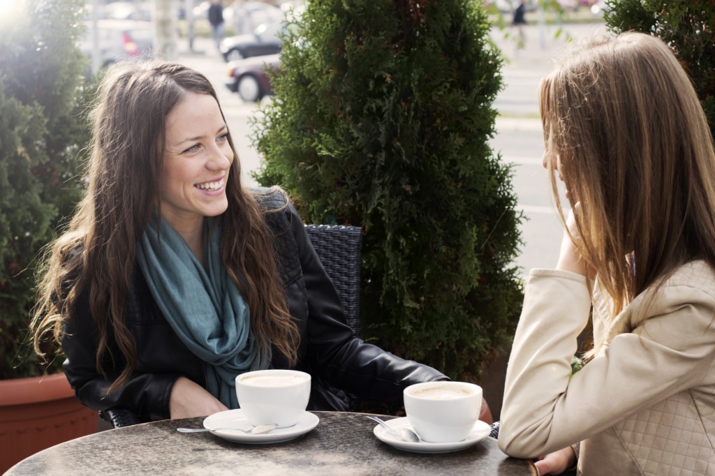 Two young women sitting in cafe and chatting outdoors.