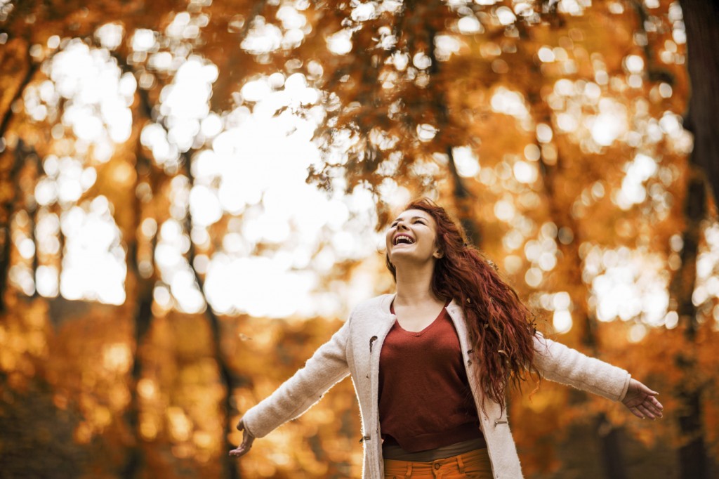Cheerful redhead woman enjoying in autumn day in the park.