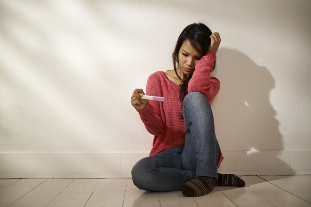 Sad girl sitting on floor looking at pregnancy test