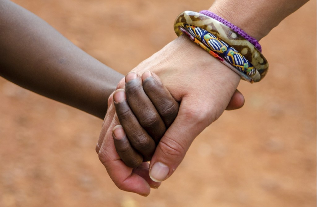 A black child and a white woman hold hands.