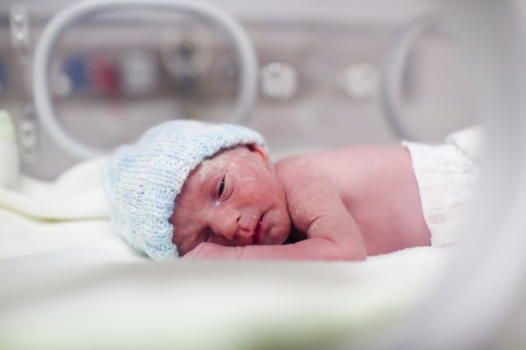 Newborn boy covered in vertix in incubator