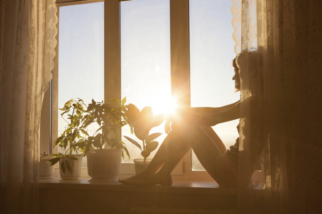 Woman sitting by window watching the sun rise