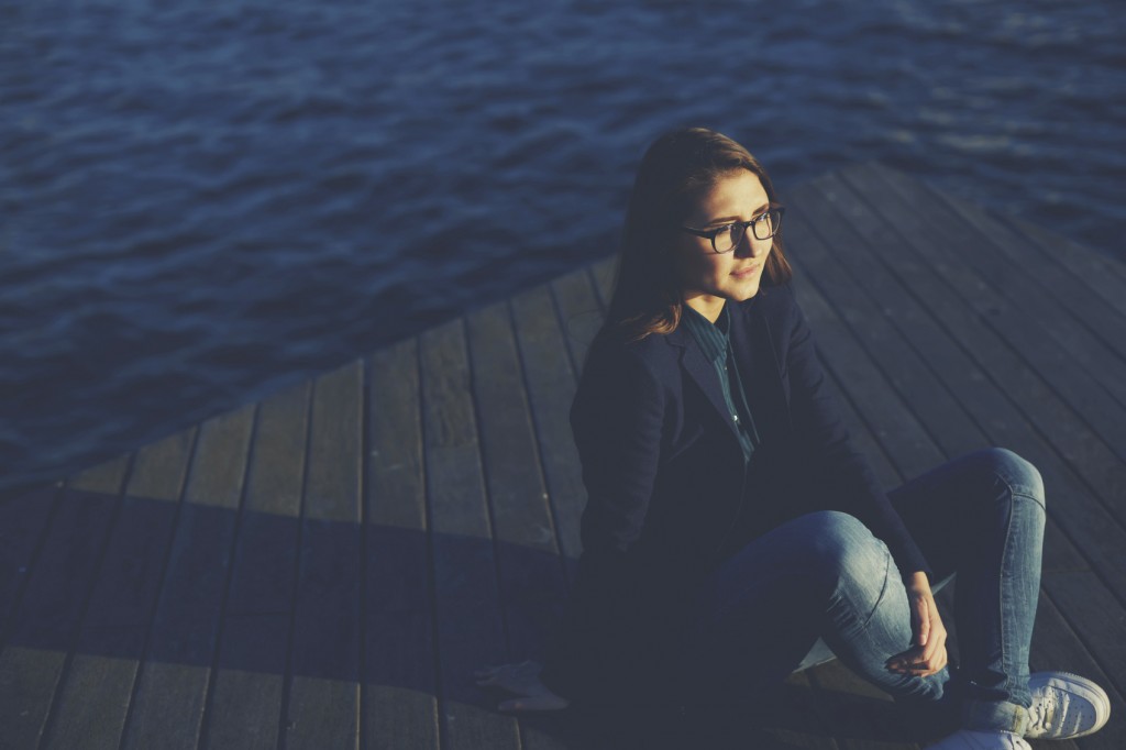 Portrait of a young woman sitting on a pier and admitting beautiful view