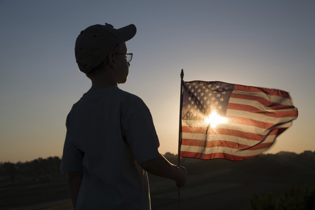 boy holding American flag watching the sun set.
