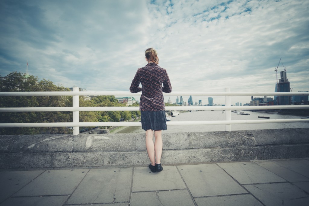 A young woman is standing on a bridge in the city and is admiring the skyline