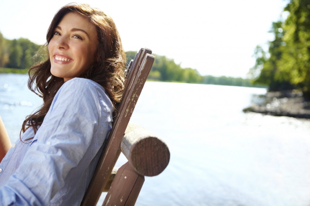 Gorgeous young woman sitting by a beautiful lake on a summer's day -