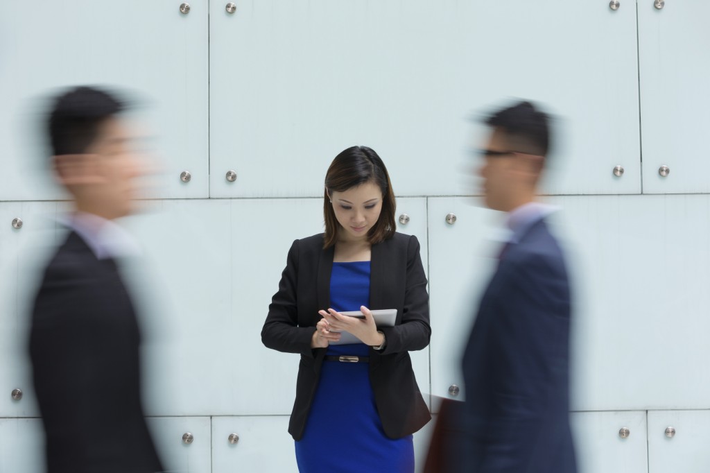 businesswoman using tablet surrounded by people rushing pa
