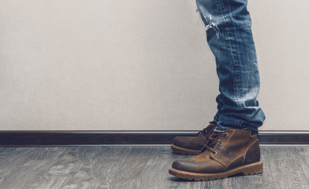 Young man's legs in jeans and boots on wooden floor