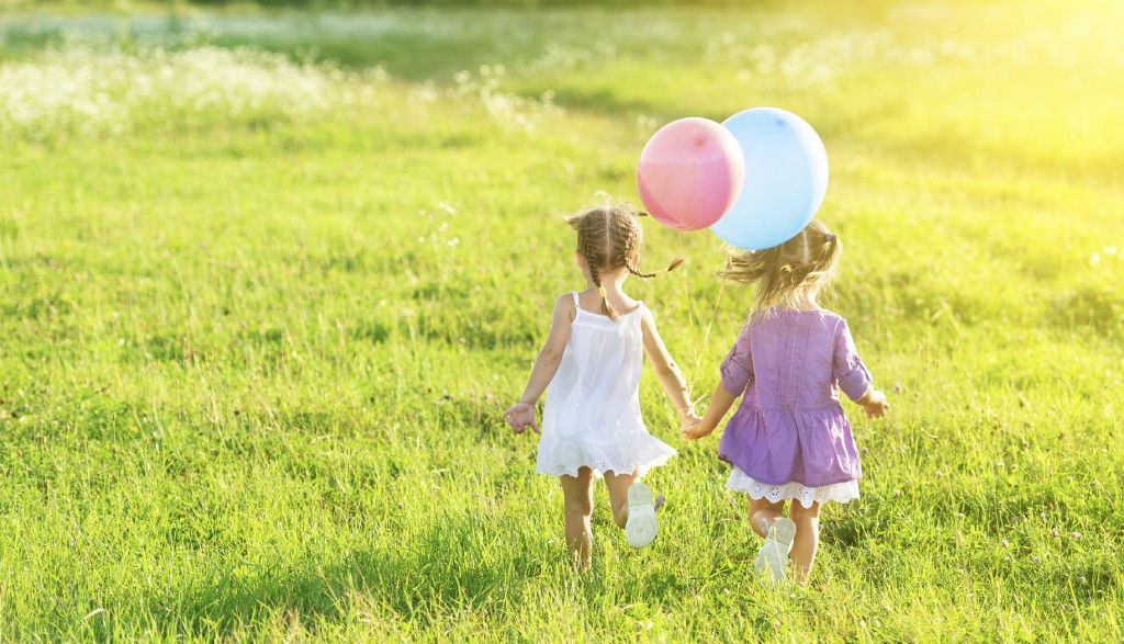 happy girls twin sisters with balloons in summer field on nature