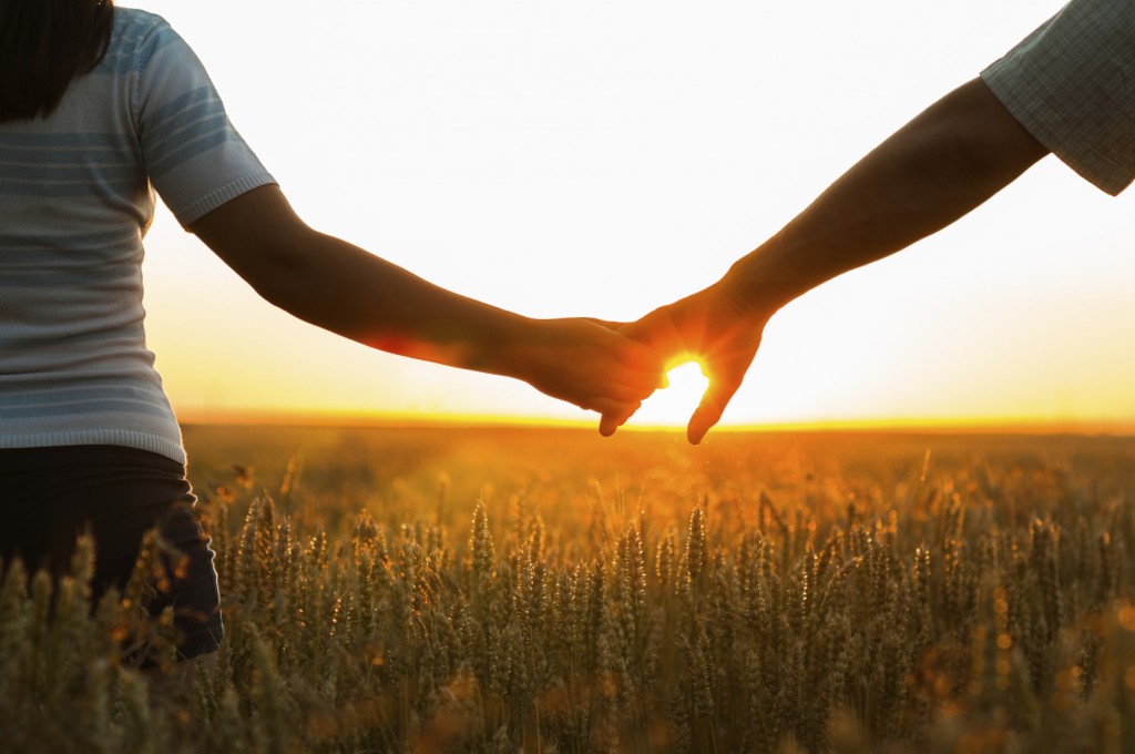 Young couple holding hands in the wheat field on sunny summer day.