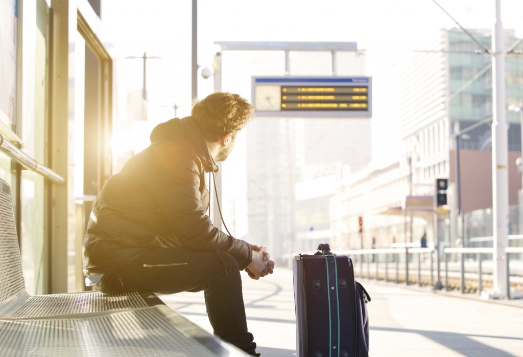 Young man sitting at train station looking at time schedule