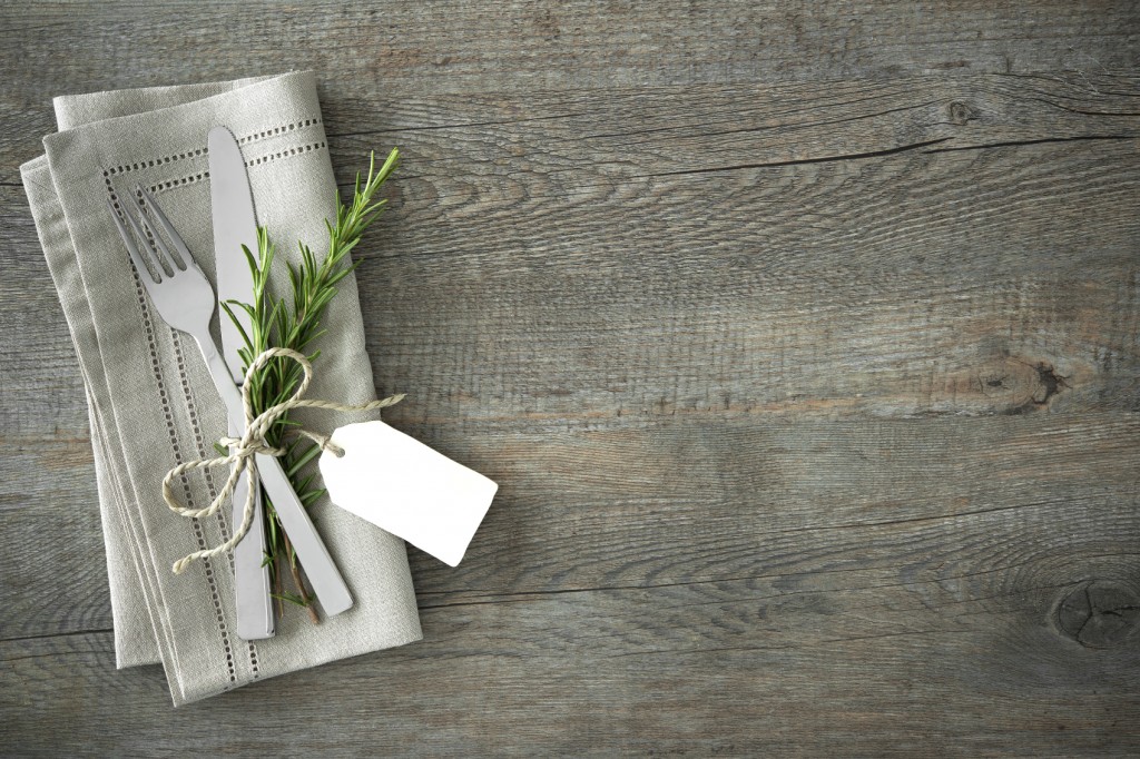 Silverware with a twig of rosemary and empty tag on rustic wooden background