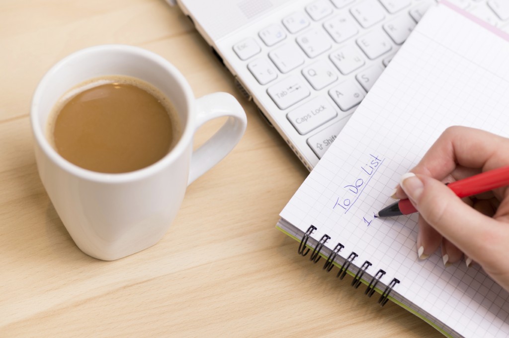 To do list. Woman writing a 'to do list' at her desk with a cup of fresh coffee