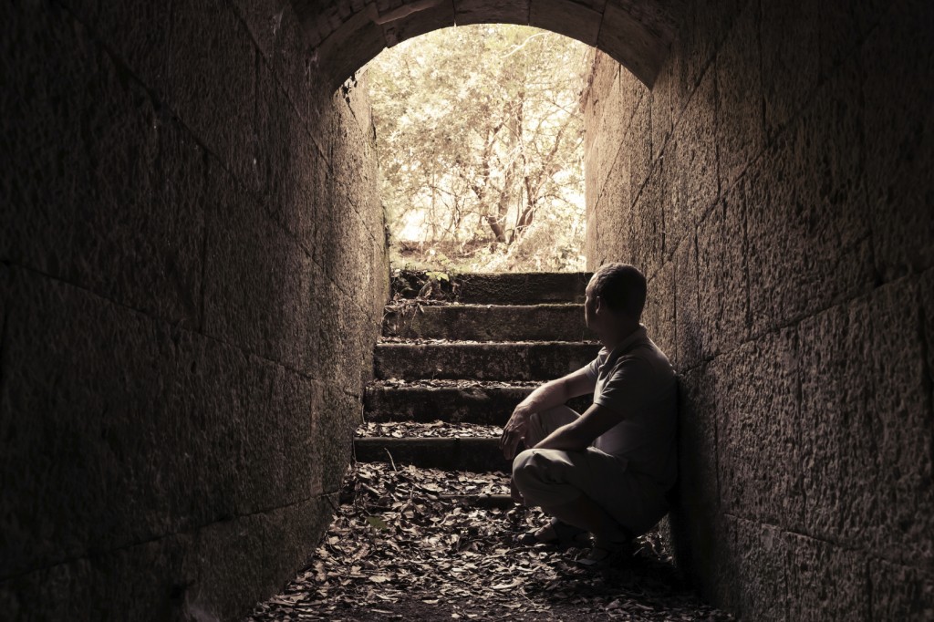 Young man sits inside of dark stone tunnel