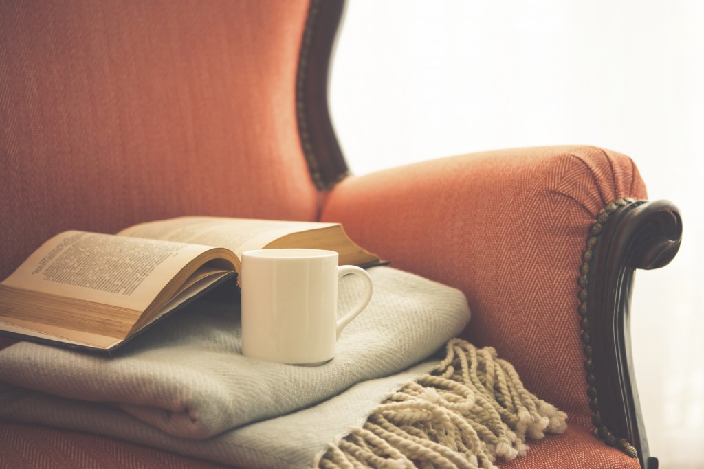 Book, cup and warm plaid on cozy retro armchair.