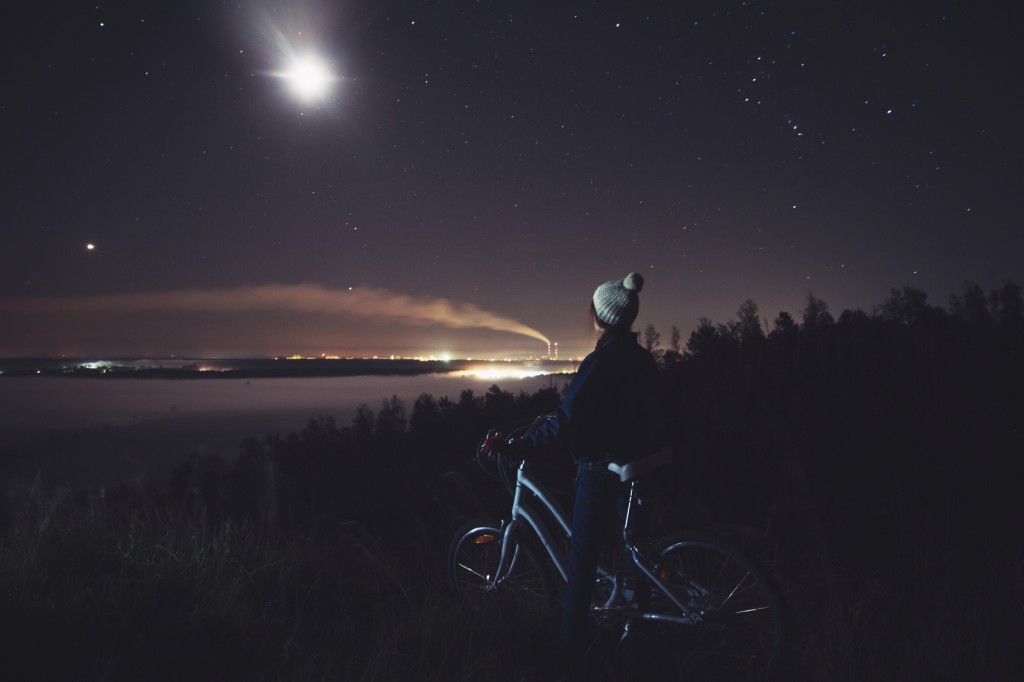 Woman with a bicycle looking at the night landscape