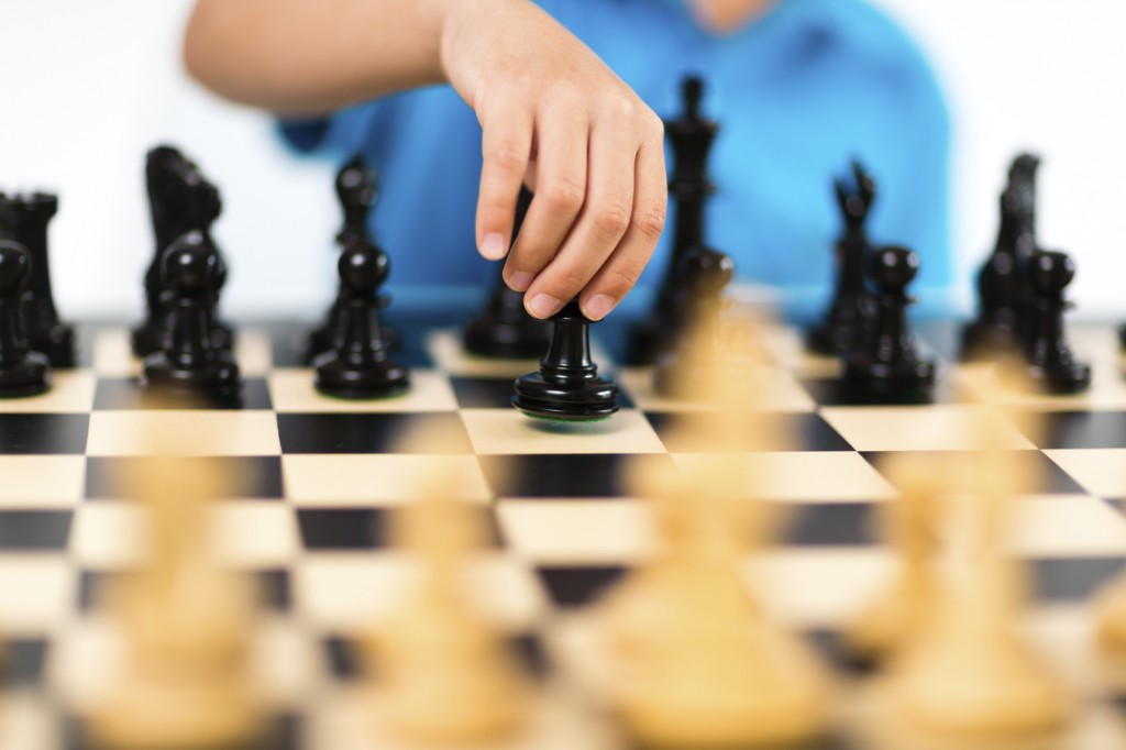 Young caucasian boy playing chess on white background.