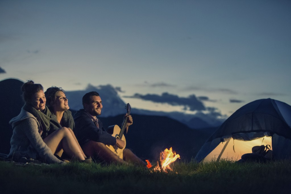 Three friends camping with guitar singing on mountain at night